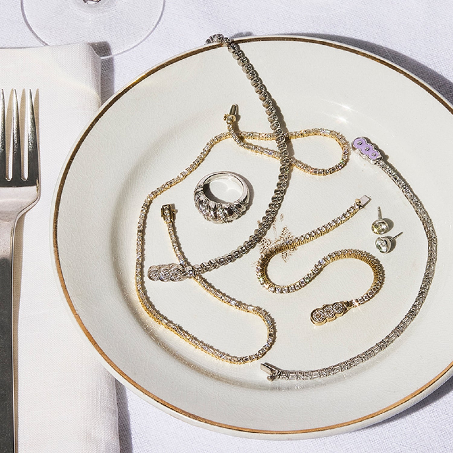 A dinner plate decorated with Petite Frites 18K yellow and white gold diamond tennis bracelets, rings and earrings. The image highlights the playful, bold, and luxurious designs of Petite Frites’ collection.