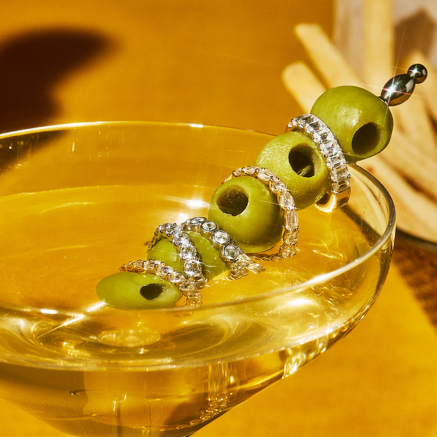 Petite Frites eternity rings stacked on a martini olive skewer in a dirty martini glass.