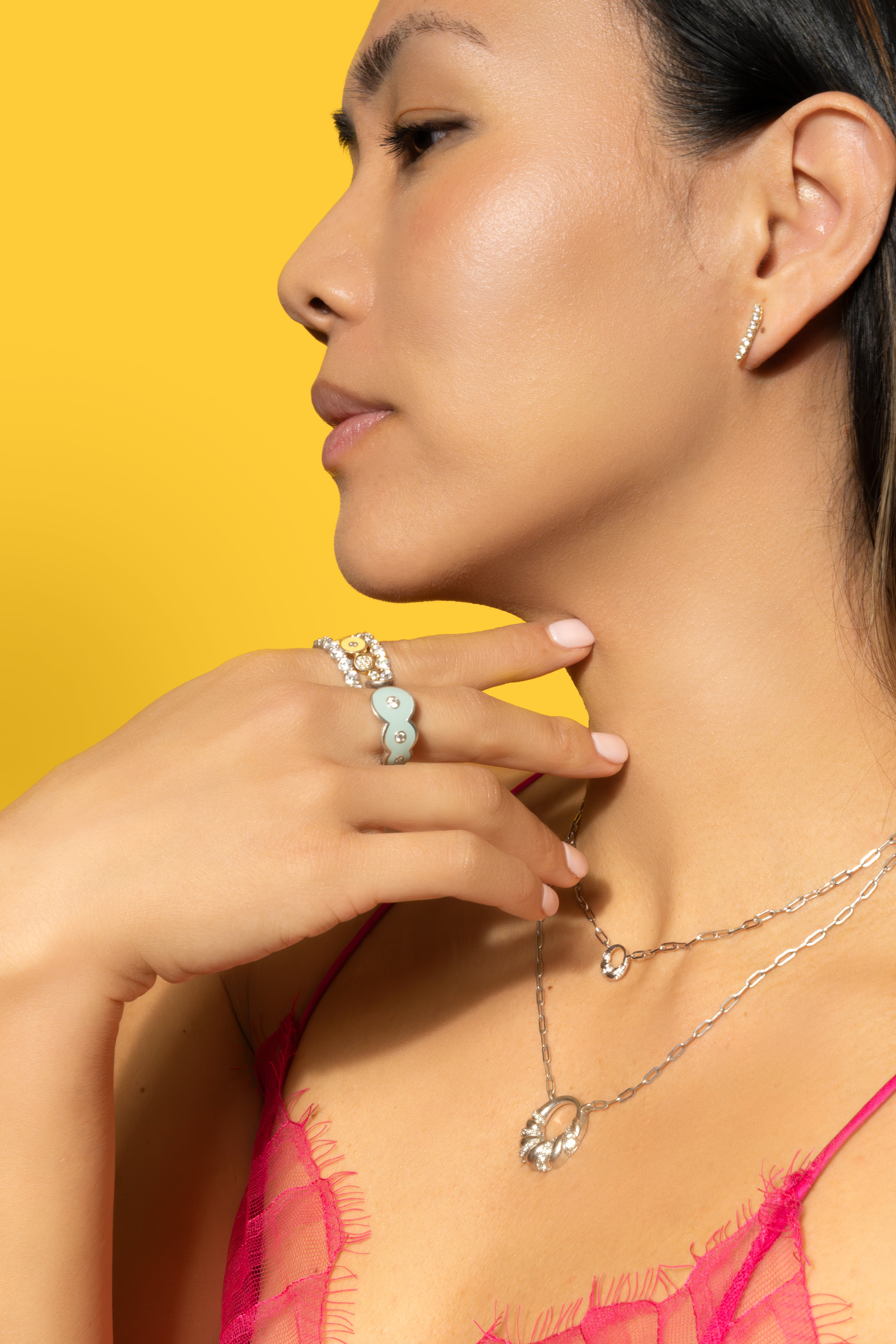 Petite Frites 18K gold and diamond jewlery on a model with a bright yellow background. Model is wearing Frites Earrings, Martini Ring, With a Twist Necklace, Champagne Ring, and Eternity Bands