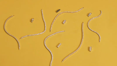 Petite Frites bracelets and clasps strewn across a yellow table. A hand comes in to pull one of the bracelets down towards them.